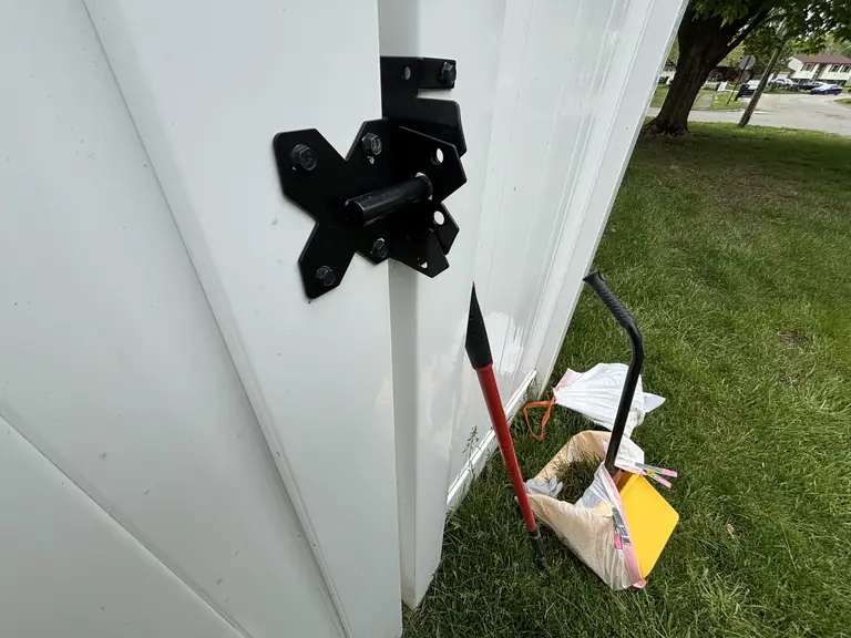 Real visit photo: a closed white gate latch with the scooping tools and a tied bag.
